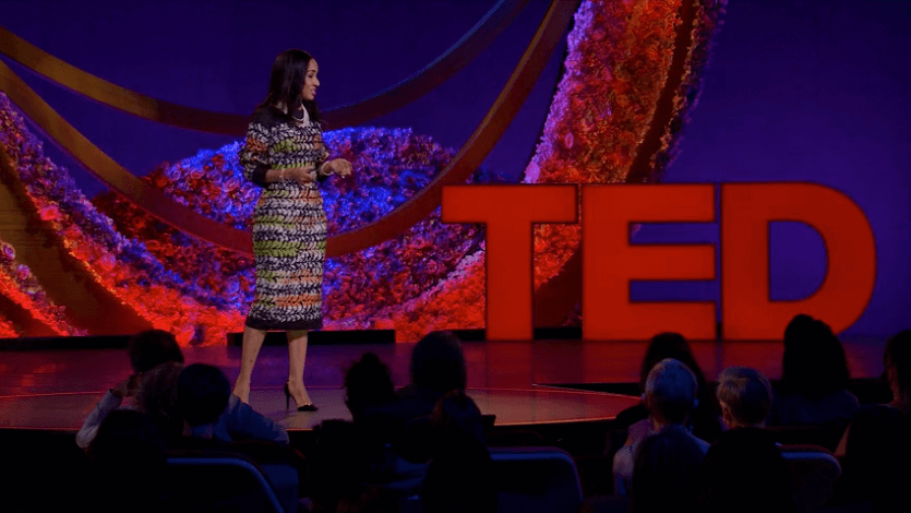 A woman standing onstage with an audience and the word "TED" in the background
