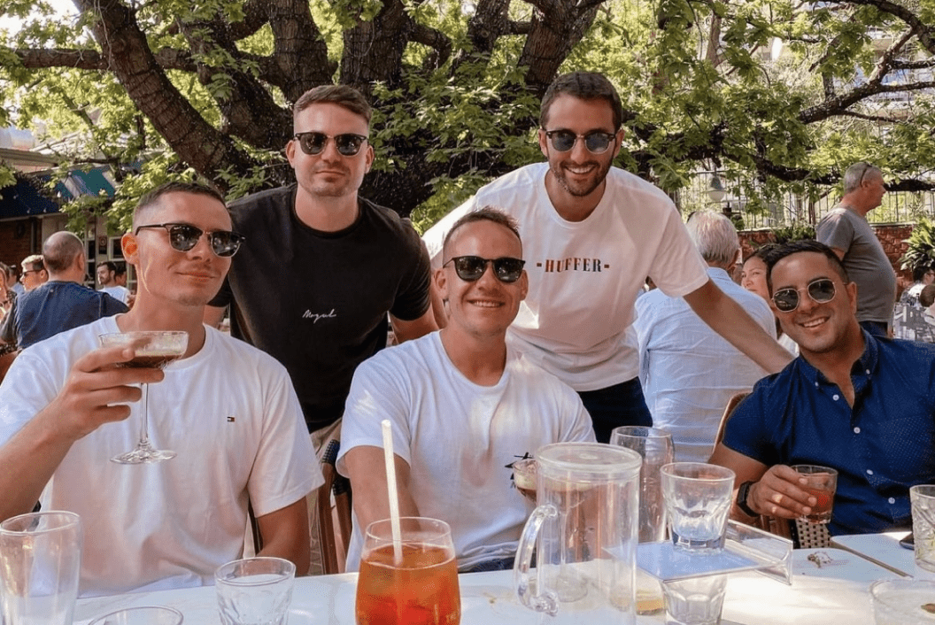 A group of men wearing sunglasses outside and smiling