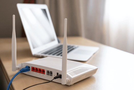 An internet router sits on a table near an open laptop.