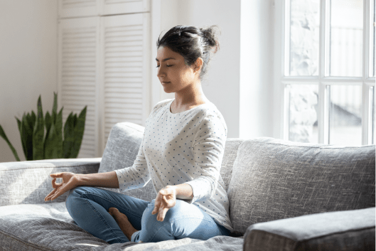 A woman sits cross legged on her couch while meditating