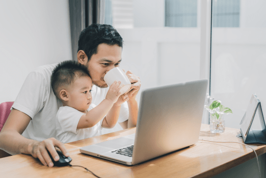 A man drinks coffee with his child while looking at a laptop screen