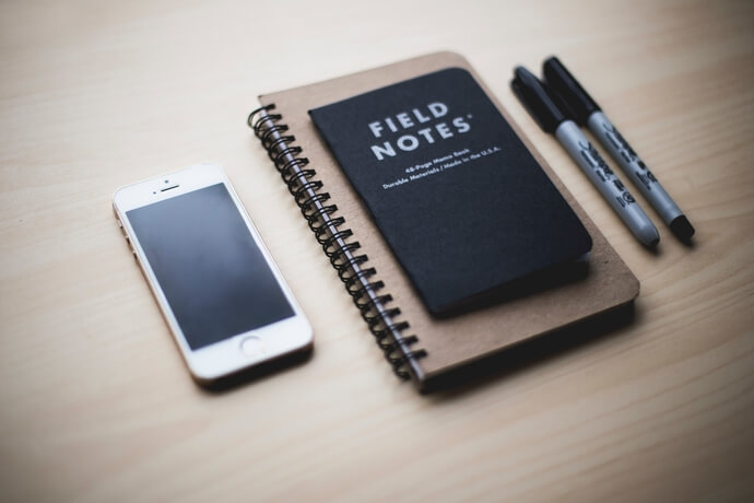 Photo d'un téléphone portable avec deux carnets de notes et des stylos.